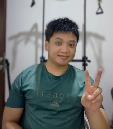 Asep in a green T-shirt, smiling and holding up a peace sign.