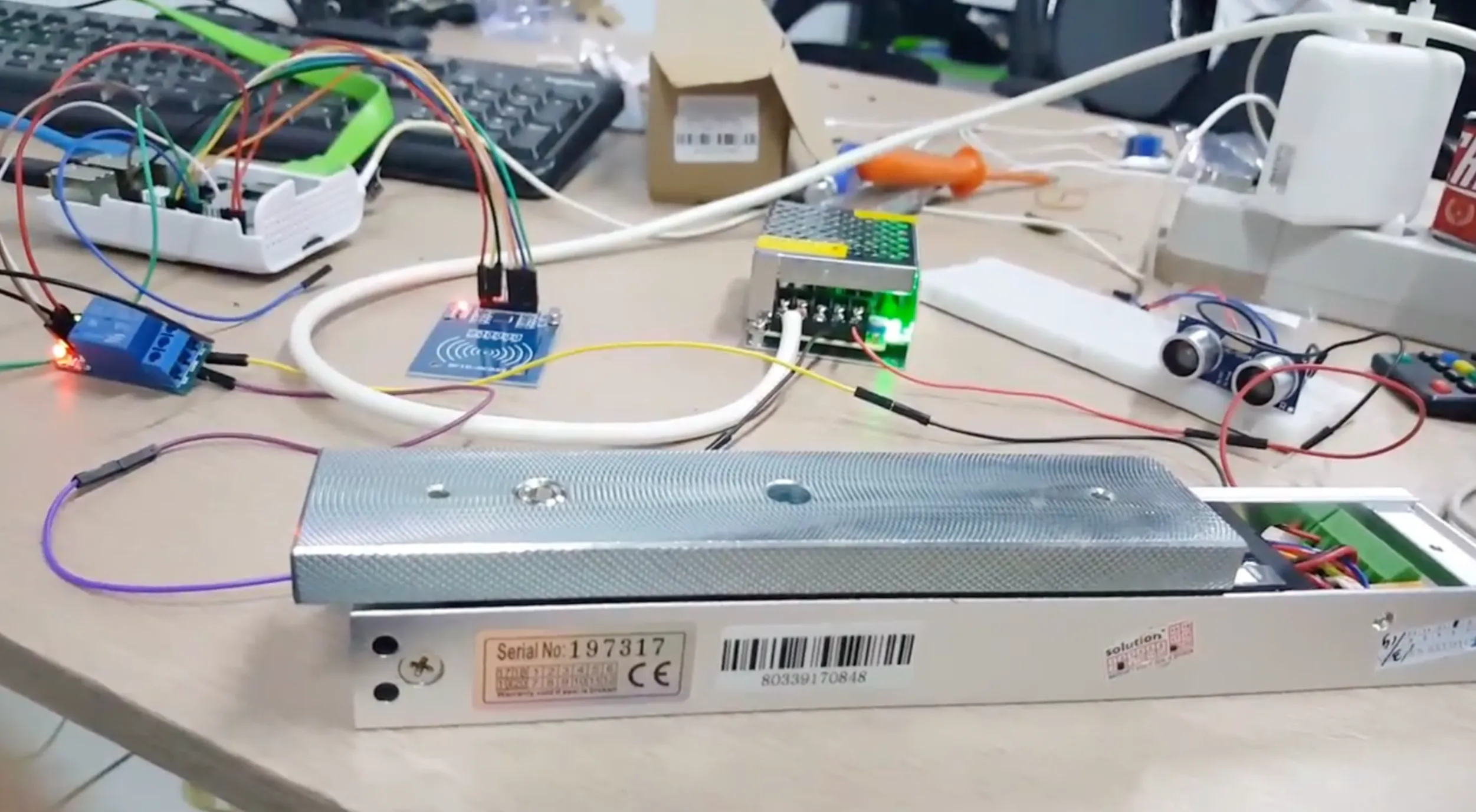 The prototype hardware on a desk: a Raspberry Pi, RFID reader, relay, power supply, ultrasonic sensor, and electromagnetic door lock.